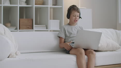 little boy is talking to someone by online video call using notebook with internet and headphones staying home at vacation