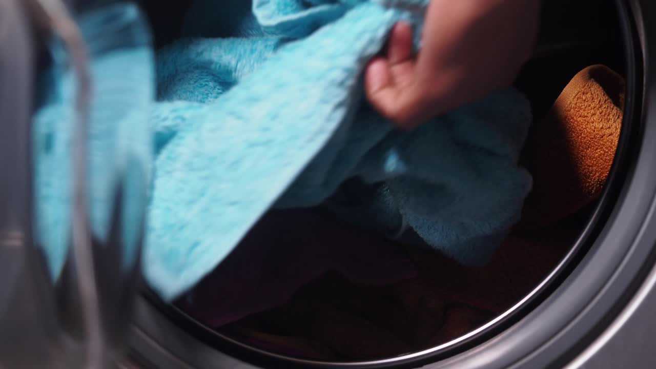 A person loading colorful towels into a washing machine