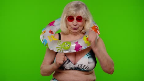 Mature-woman-traveler-dancing,-celebrating,-posing-with-rubber-ring-in-swimsuit-bra-on-chroma-key