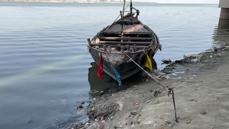 closeup view of weathered wooden boat resting on a muddy shoreline, partially in the water in ganga, patna.