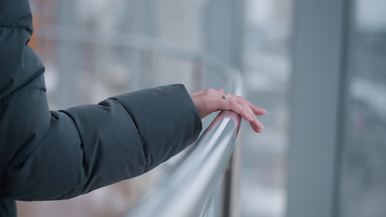 그녀가 걸어가는 동안 레일에 놓인 반지와 함께 여성의 손의 클로즈업, 현대적인 건물 유리 배경으로 도시 환경에서 세련되고 현대적인 느낌을 제공합니다.