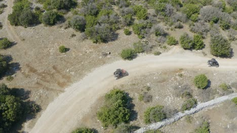 Aerial-follow-shot-of-buggy-cars-riding-on-rough-and-unpaved-terrain-amidst-barren-land