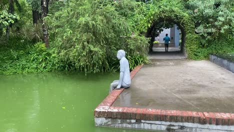 Eine-Statue-Eines-Mannes,-Der-In-Der-Nähe-Eines-Teichs-In-Einem-Park-Sitzt
