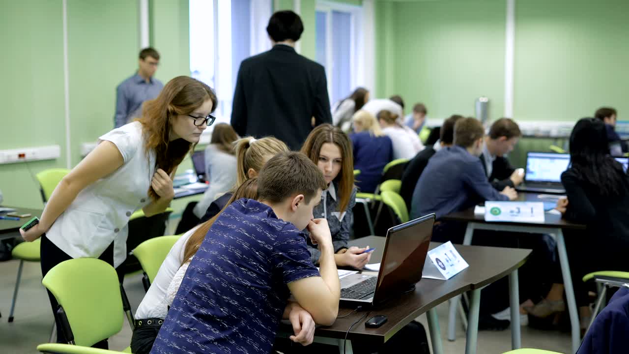 estudiantes en la universidad en el examen de ciencias de la computación. en la gran audiencia una gran cantidad de gente y unas pocas computadoras portátiles en las mesas. chica mira en la computadora portátil