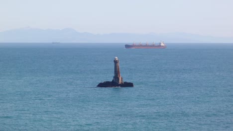 high angle view of the karori rock lighthouse with a cargo ship slowly passing in the background