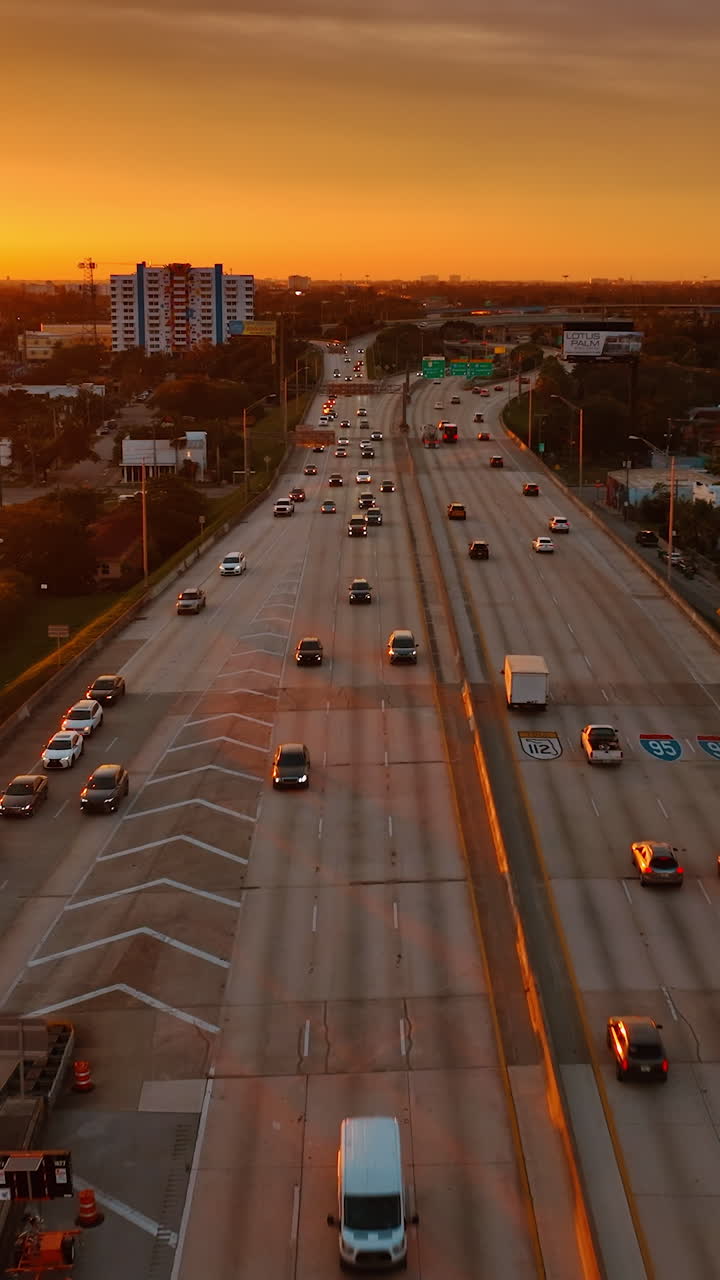 Flying above the multi-lane road at sunset. Orange light of setting sun covering the scenery of Miami, Florida, USA. Vertical video