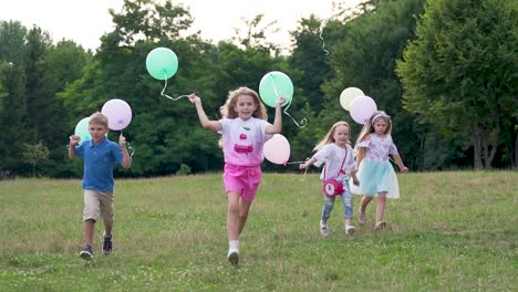 group of children run in the park on the grass. cheerful children with balloons in their hands. slow motion