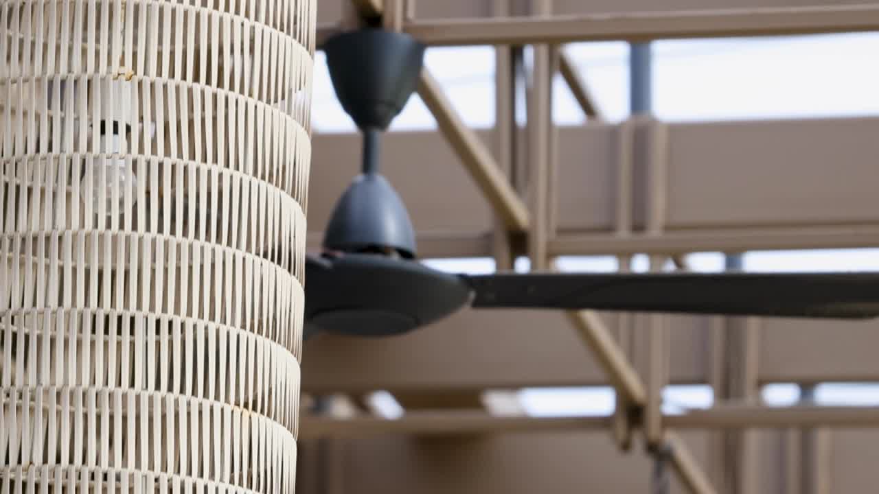 Ceiling fan spins slowly in a bright, modern hotel atrium with wicker decor and natural lighting