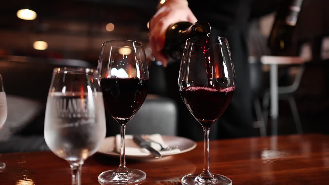 Una mano versa vino rosso in un bicchiere accanto all'acqua, ristorante elegante, illuminazione calda, messa a fuoco selettiva