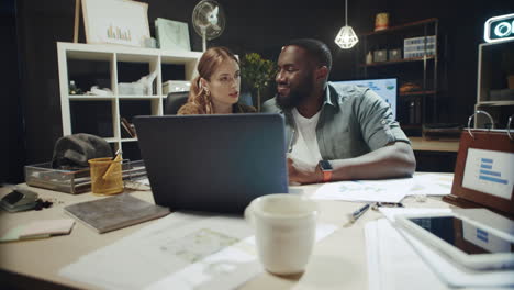 afro man and hipster woman talking about solution on laptop screen in office.