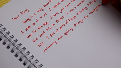 scrivere a mano un diario con una penna rossa colpo di testa primo piano della mano della donna
