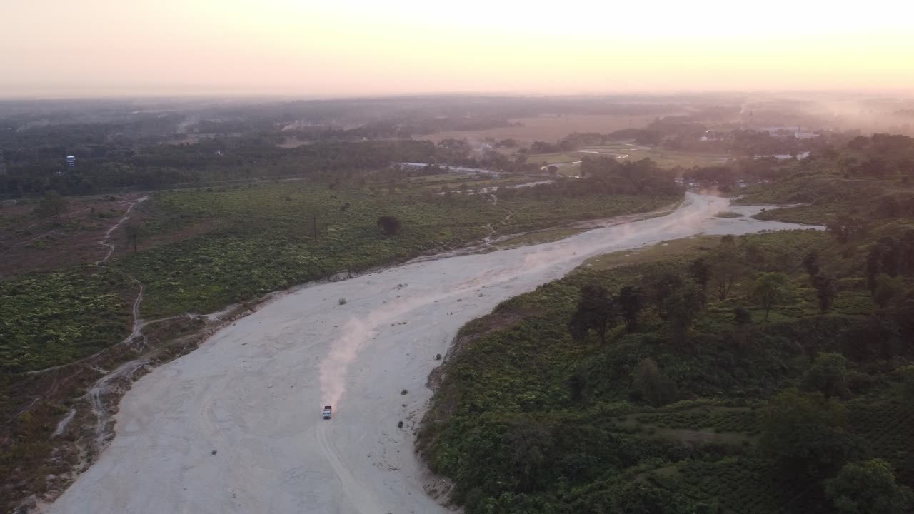 Illegal sand mining on dry Torsa River causing dust generation in winter near Bhutan border surrounding tea estate and forest lands, West Bengal, Drone view