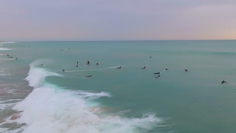 Stunning pastel sunset sky on clean ocean wave breaking on surfers with ocean mist