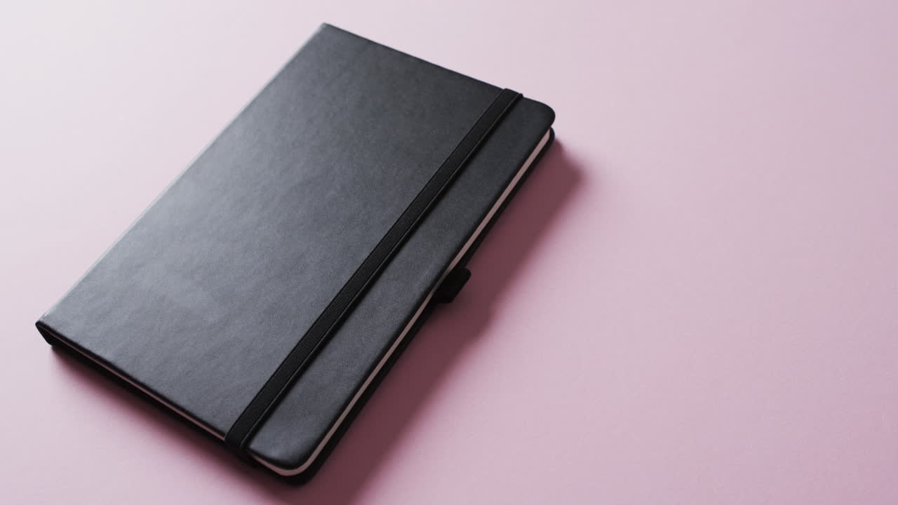 primer plano de un cuaderno negro cerrado con espacio de copia en un fondo rosa en cámara lenta
