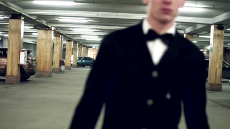 Young-businessman-in-a-black-suit-with-bow-tie-walking-on-the-parking-with-big-leather-bag.-Slow-Motion