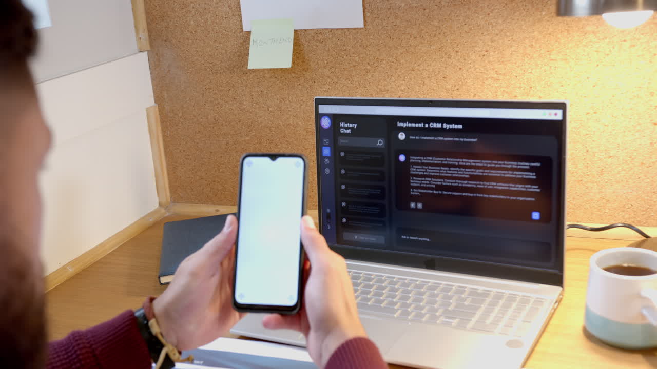 Using smartphone and laptop for AI chatbot, man working from home at desk, copy space