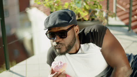 plano medio del hombre feliz acostado en el balcón abierto y comiendo donut