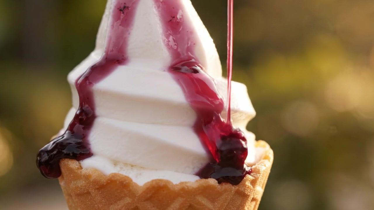 Geniet van Elke Hap: Een Close-up van Romig Softijs met Heerlijke Bessensaus die over een Wafelhoorntje Druppelt, Perfect voor een Zomerse Traktatie.