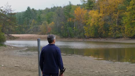 Adult-Male-Overlooking-River-Flowing-Through-Autumn-Tree-Forest