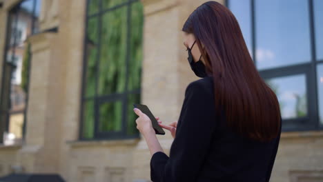 Masked-lady-using-mobile-phone-in-downtown.-Businesswoman-checking-email-phone