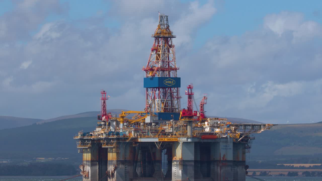 Kameraet zoomer støt ud fra offshore-olieboringsplatform under dagslys og afslører kystlandskabet