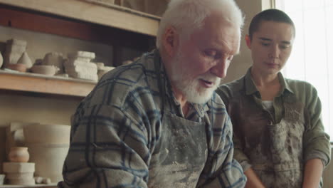 elderly potter giving ceramics class to young woman