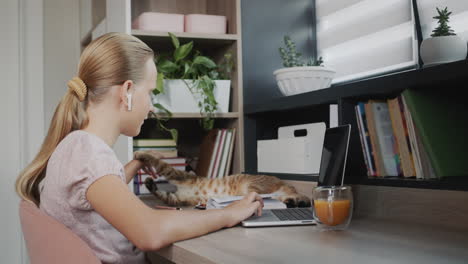 La-Niña-Está-Ocupada-Con-Una-Computadora-Portátil-En-Su-Habitación,-Junto-A-Ella-Hay-Un-Gato-Rojo