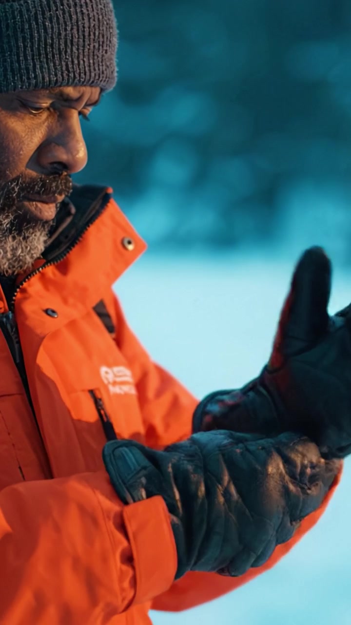 A man dressed in winter gear stands against a snowy backdrop, showcasing resilience and determination in a harsh, cold environment during an outdoor adventure.