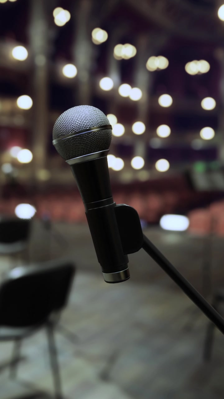 Microfono posizionato davanti a sedie vuote con luci in un teatro di notte.