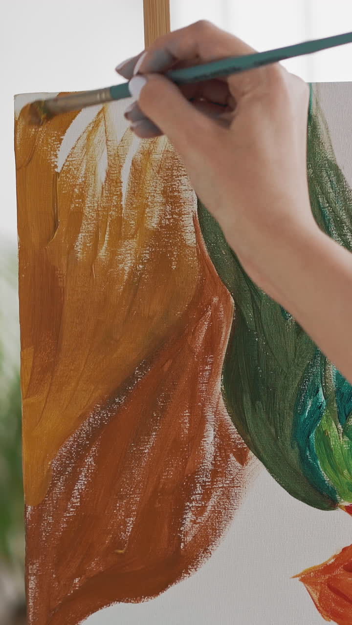 Talented female artist makes orange strokes drawing tropical plant on white canvas in light art studio extreme close backside view