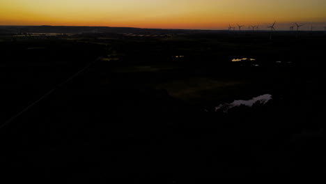 toma aérea - volando lentamente lejos del parque eólico al atardecer, silueta de turbinas eólicas en el fondo del cielo naranja, disco, pomorskie, polonia