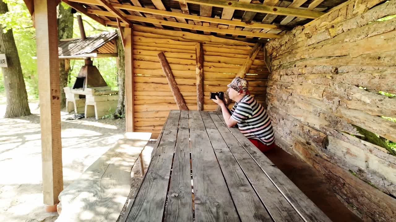 노인 사진작가는 여름 숲의 피크닉 테이블에 앉아서 사진을 찍었습니다.