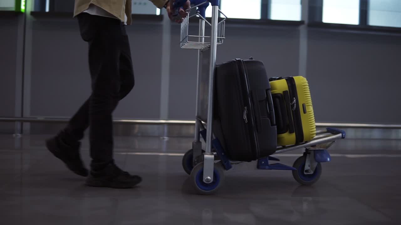passager masculin méconnaissable avec chariot à bagages à l'aéroport international. marche dans la précipitation, vue latérale