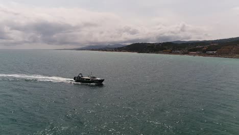 Aerial-Shot-of-a-Boat-Moving-Across-Water-Near-Shore-Line-on-a-Calm-Clear-Day