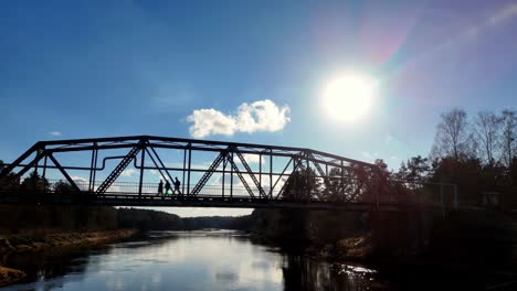 Aerial-panoramic-sun-shining-below-people-crossing-river-above-water-channel-countryside-landscape