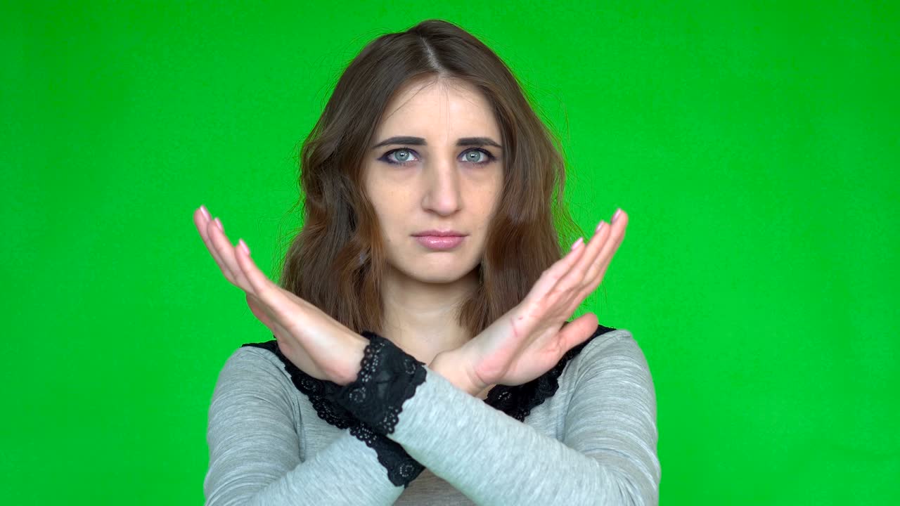 Young woman showing a stop arms crossed while looking at the camera over green background.