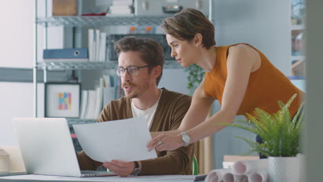 male and female architects in office working at desk on laptop and looking at plans