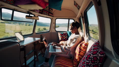 woman working on laptop inside a custom camper van with her dog, enjoying a scenic view