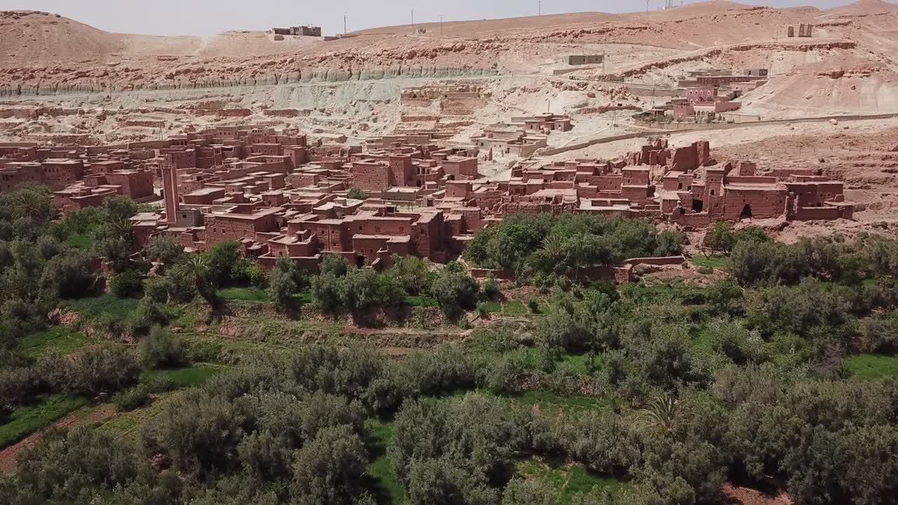 ワルザザートのヤシの木と農地がある緑豊かなオアシスの上に建てられた密集した砂漠の村のドローン空撮。旅行、環境、ドキュメンタリー映像に最適な強い高低差。