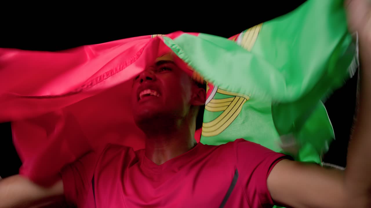 Adult African American male shouting and waving Portugal flag in red t-shirt at studio, celebrating