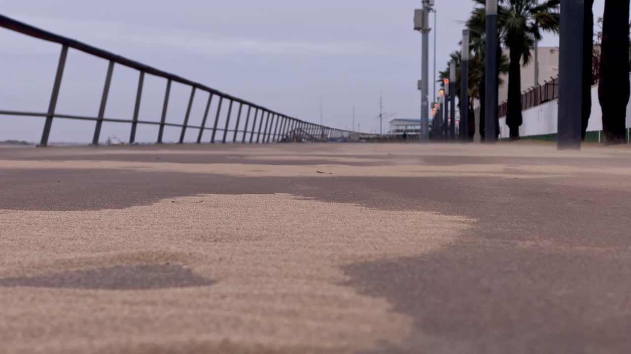 Areia soprando sobre um calçadão costeiro em um dia ventoso.