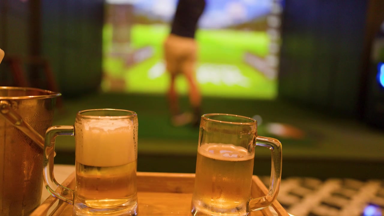 Una mano posa un bicchiere di birra lager accanto a un'altra birra mentre un golfista esegue uno swing.