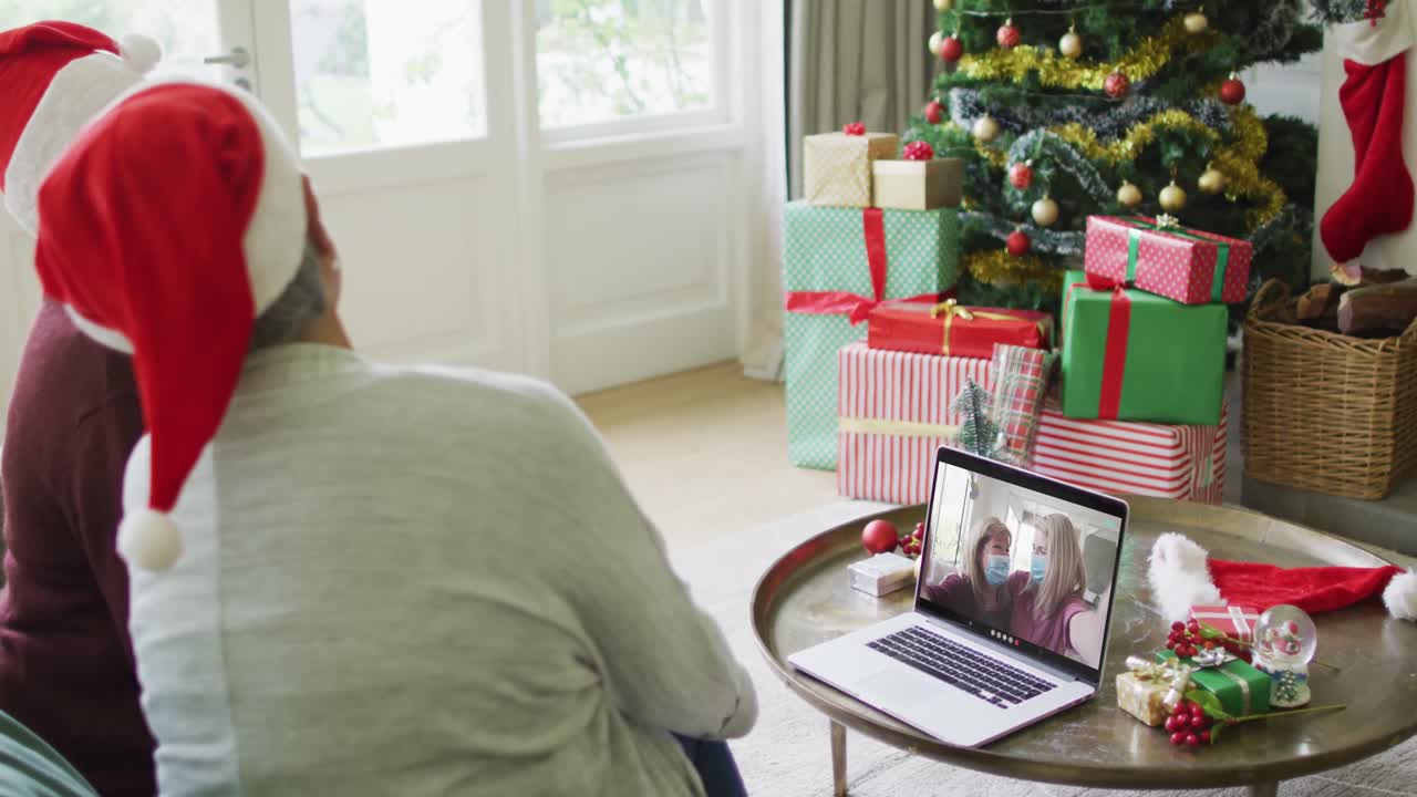 diversas amigas mayores que usan una computadora portátil para una videollamada de navidad con una familia feliz en la pantalla