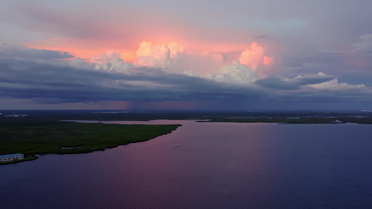 Expansive view of calm coastal water beneath dramatic storm clouds illuminated by sunset hues, showing contrast between soft color gradients and the vast peaceful horizon