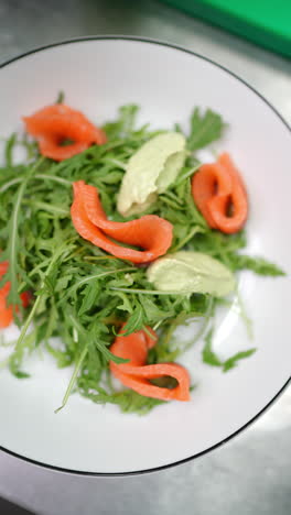 vertical footage gourmet salmon and arugula salad receiving delicate wasabi paste garnish by professional chef inside pristine restaurant kitchen environment