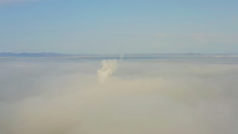 smoke from a power station chimney rising from a low, creeping fog. drone view