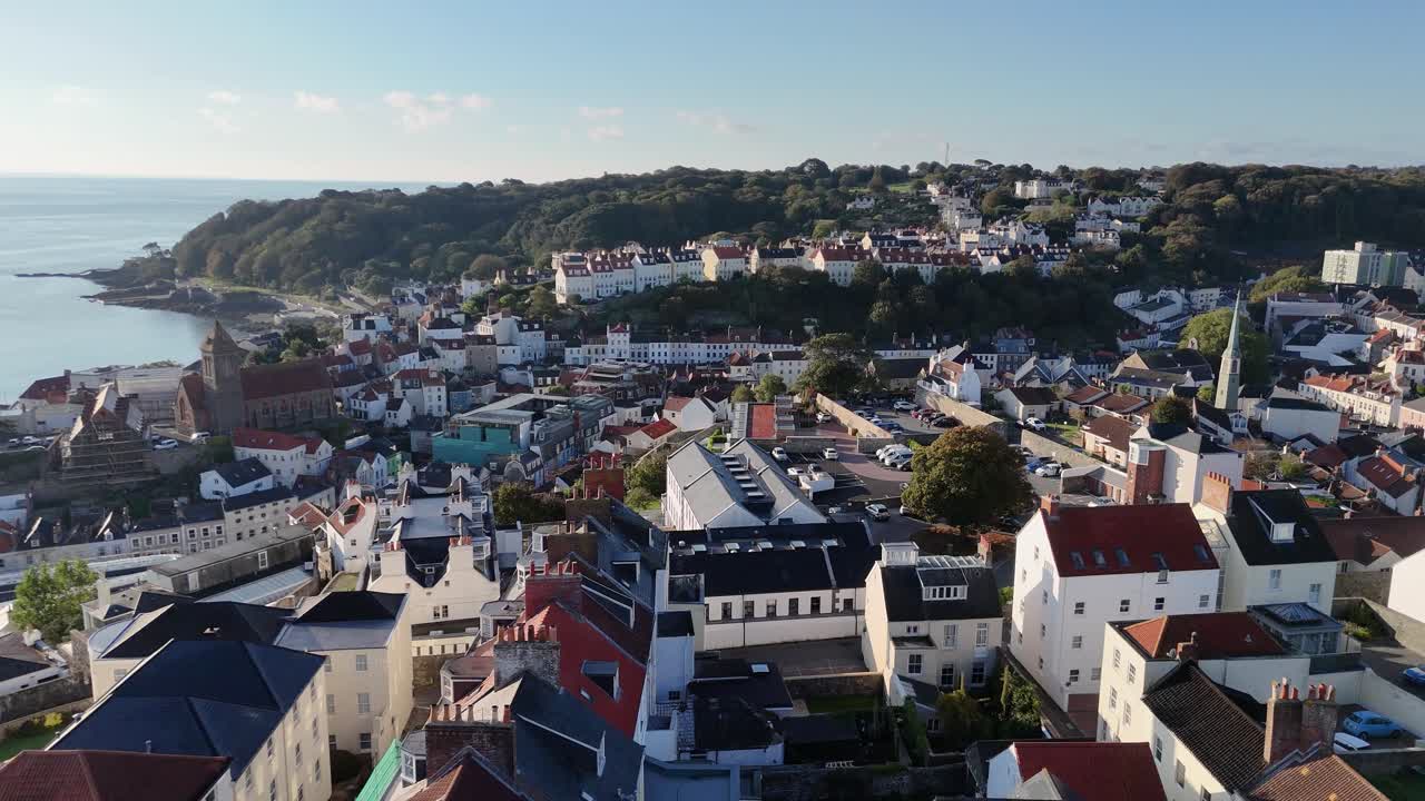 St Peter Port, Guernsey, Isole del Canale, volo a bassa quota sopra i tetti della città, volando verso sud in direzione della Baia di Havelet e delle scogliere boscose di St Martins sotto il sole del tardo pomeriggio con cielo azzurro limpido