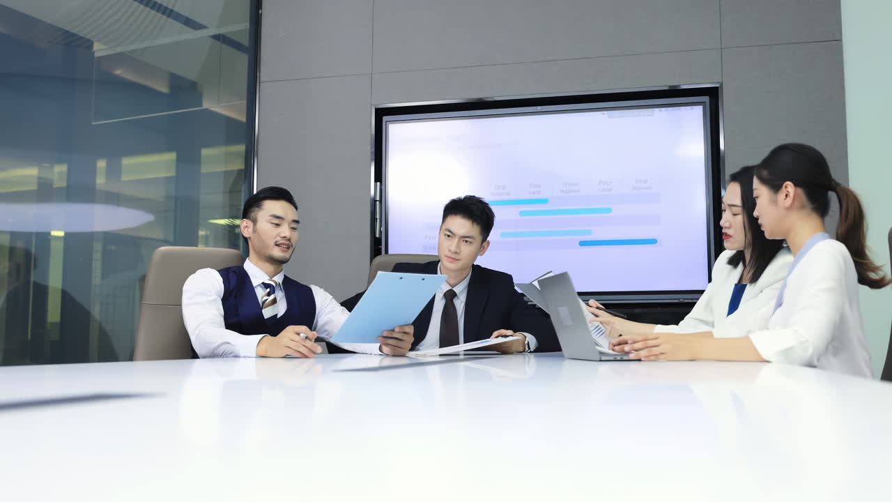 一群同事在會議室開工作會議，圍坐在辦公桌旁，聽一位男演講者講解新的營銷策略簡報並做筆記