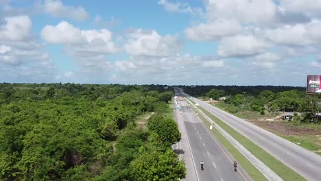 drone shot flying over a long road of the dominican republic on a sunny summer day with some cars