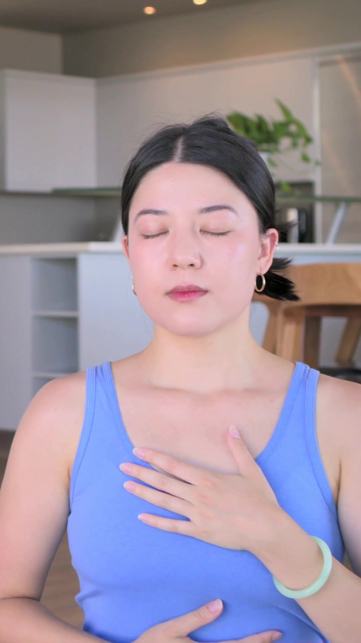 Video verticale: Pianta che si sposta, donna in completo blu che respira su un tappetino verde in cucina per la calma.